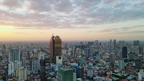 Aerial-shot-of-modern-golden-glass-skyscraper-during-construction-phase-surrounded-by-colorful-cityscape-of-Phnon-Penh