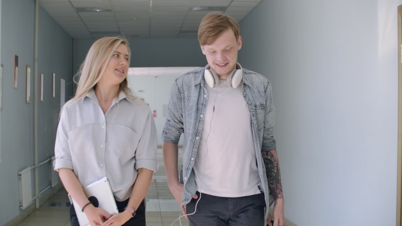 студенты колледжа идут по коридору, смеясь и разговаривая. пара парня и девушки идут в колледж.