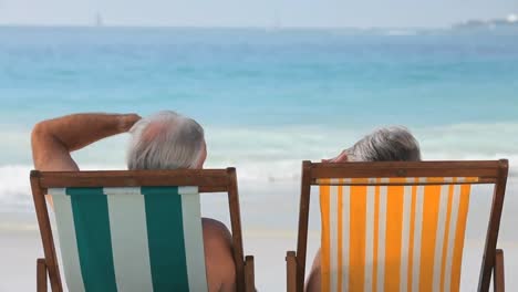 elderly couple looking at the ocean sitting on beach chairs