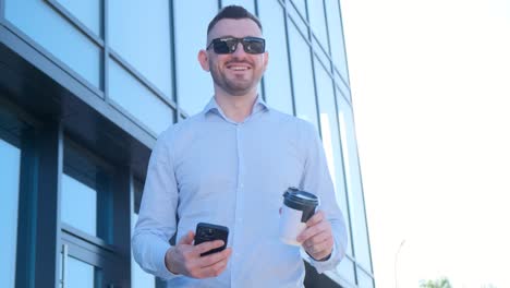 smiling rich man holding smartphone and coffee in hands while standing near his office center happy smiling rich man holding smartphone and coffee in hands while standing near his office center happy people