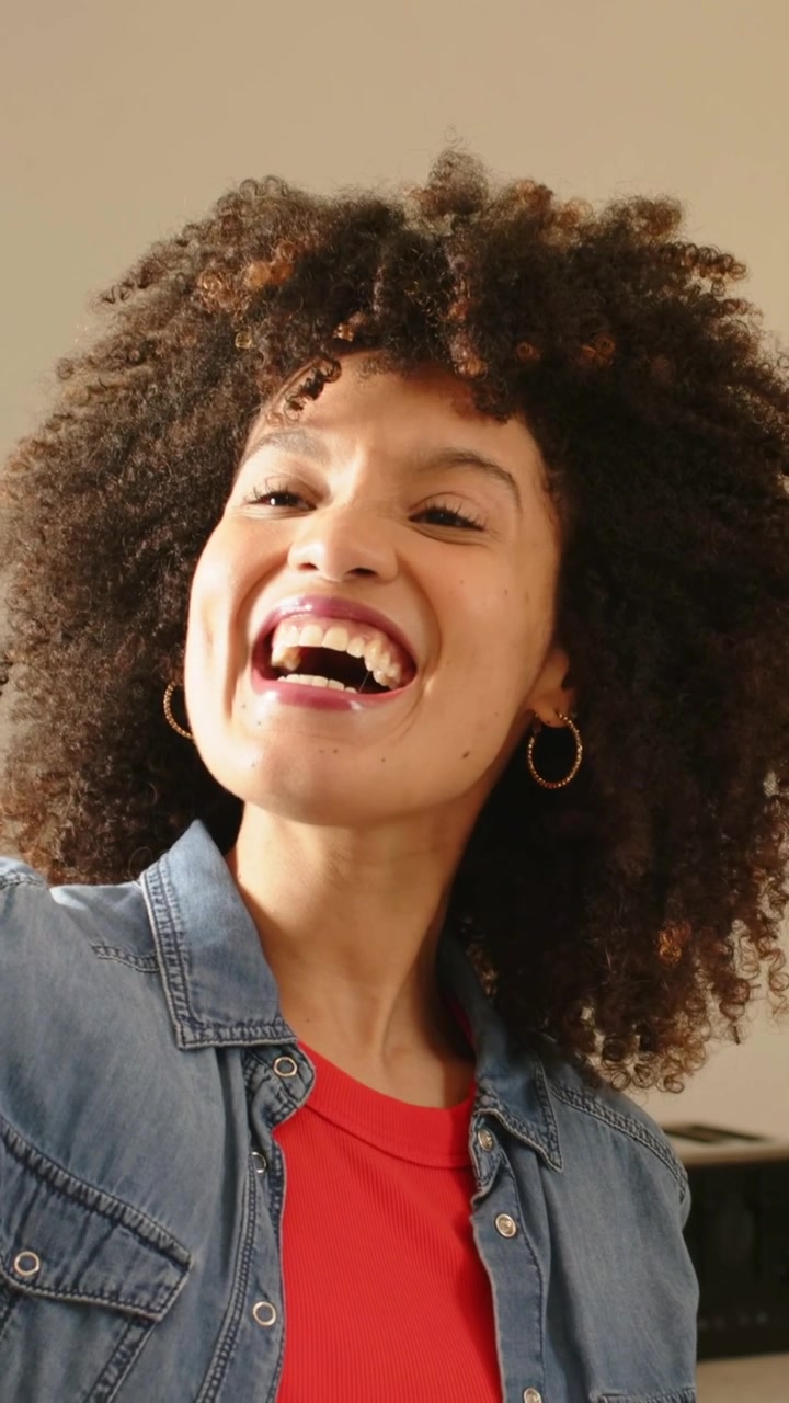 Video verticale: Donna in jeans che tiene il telefono, registra in cucina, si sposta, tocca lo schermo e ride.