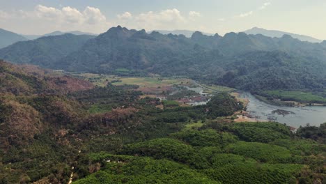 a bird's-eye view of a charming village nestled among mountains in songklaburi, thailand, portraying a serene and picturesque setting