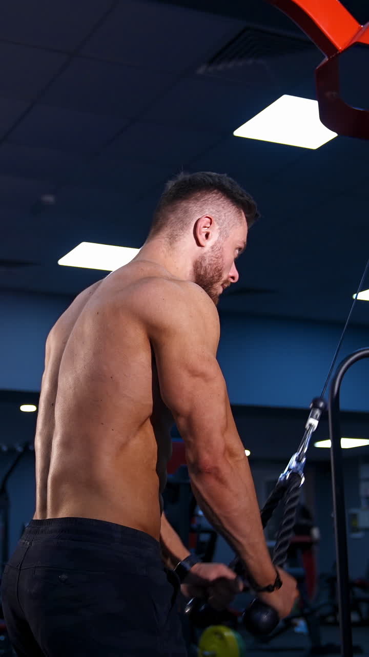 Uomo muscoloso e in forma si allena con attrezzature sportive. Giovane uomo muscoloso solleva pesi su sfondo di palestra con filtro luce blu. Video verticale.