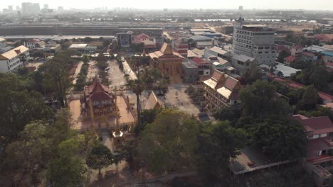 view from mekong riverbank to golden temple of phnom penh amidst cityscape - aerial wide fly-over shot