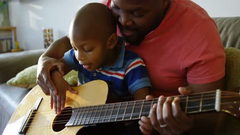 father teaching his son how to play guitar at home 4k