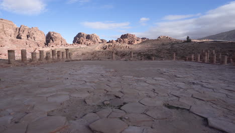 Walking-on-the-Ancient-Stone-Brick-Plaza-with-Pillars-on-Each-Side-and-Blue-Sky-and-Hills-in-the-Background-in-Ancient-City-of-Petra