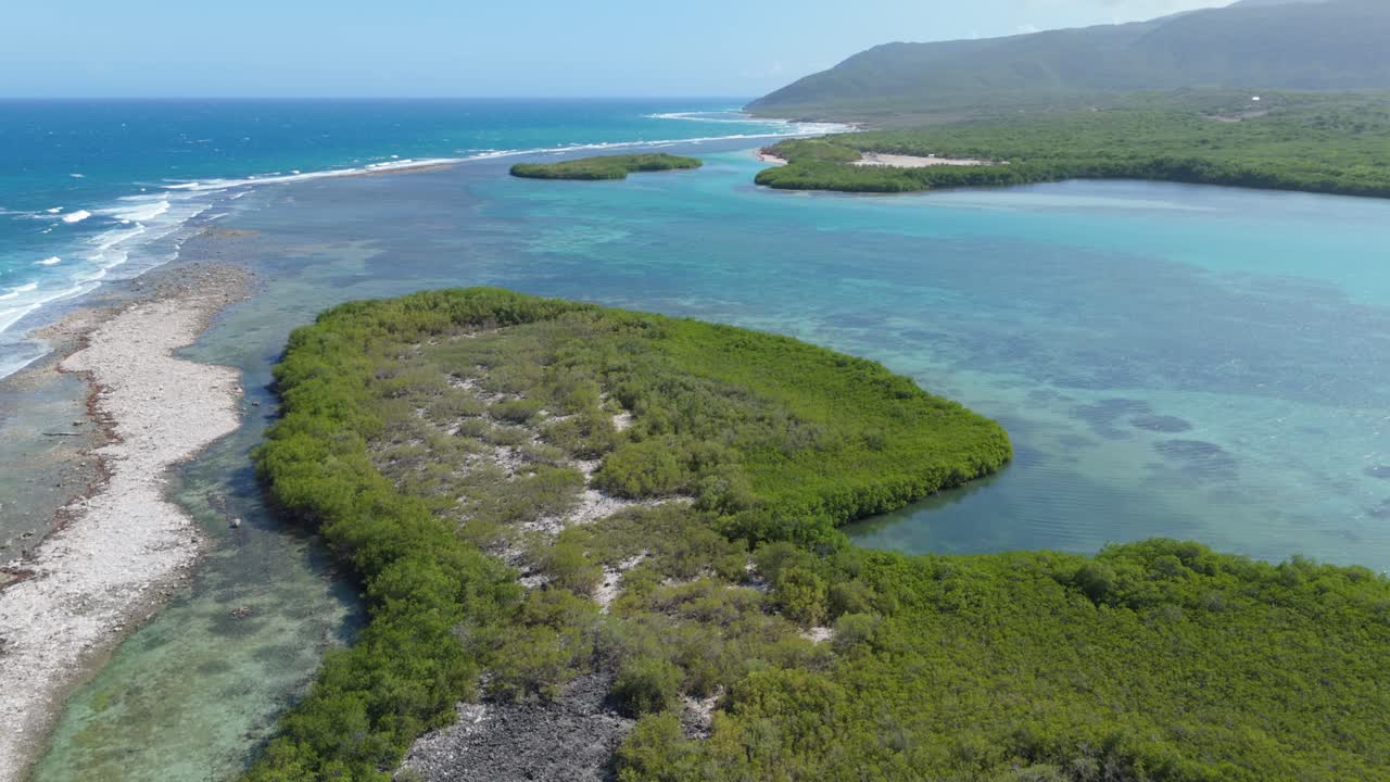 Blues Caribbean sea with breaking waves and turquoise lagoon surrounded by green islands. Aerial rising wide shot. tropical beach of Playa Caobita, Dominican Republic.