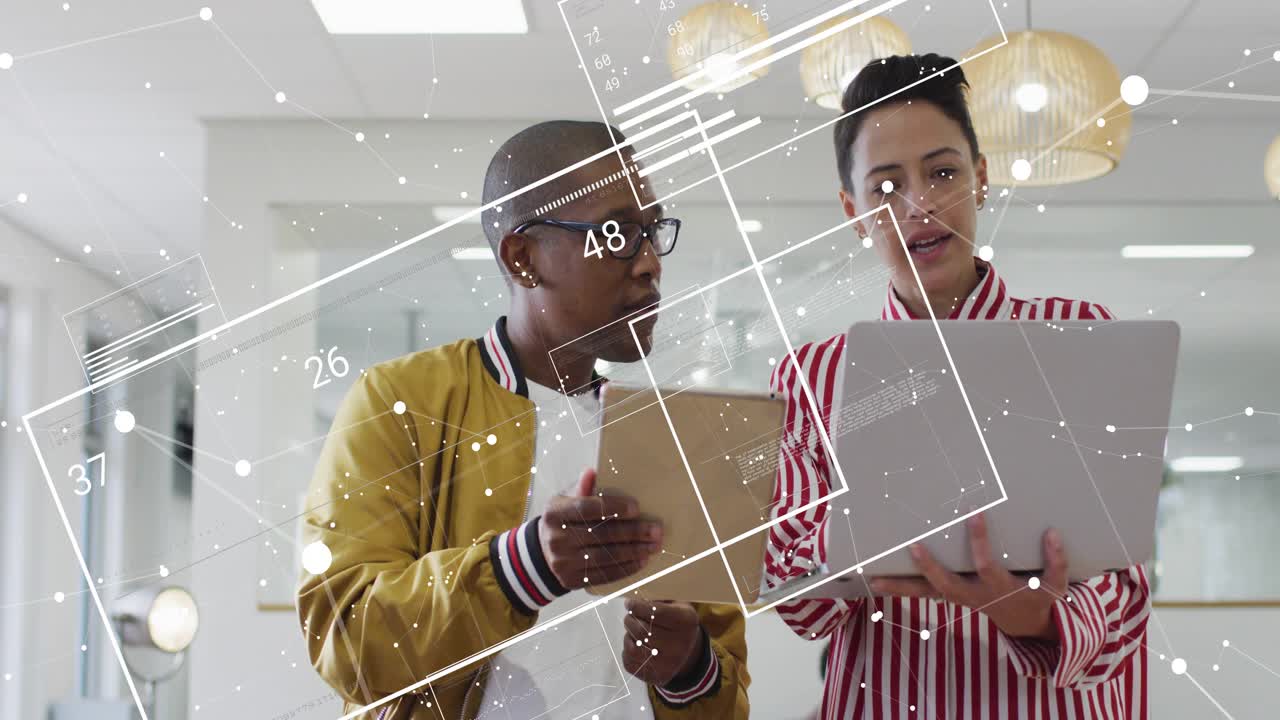 Mand tapper på tablet og opdaterer data, mens kvinde scroller igennem diagram-overlejringer på bærbar computer under en forretningsanalyse.
