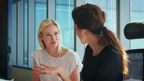 two businesswomen working at desks have discussion together