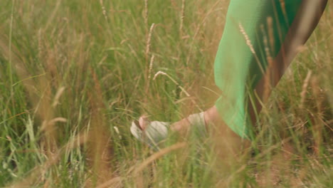 close side view of woman in green gown walking across tall grassy meadow under warm daylight, highlighting connection with nature