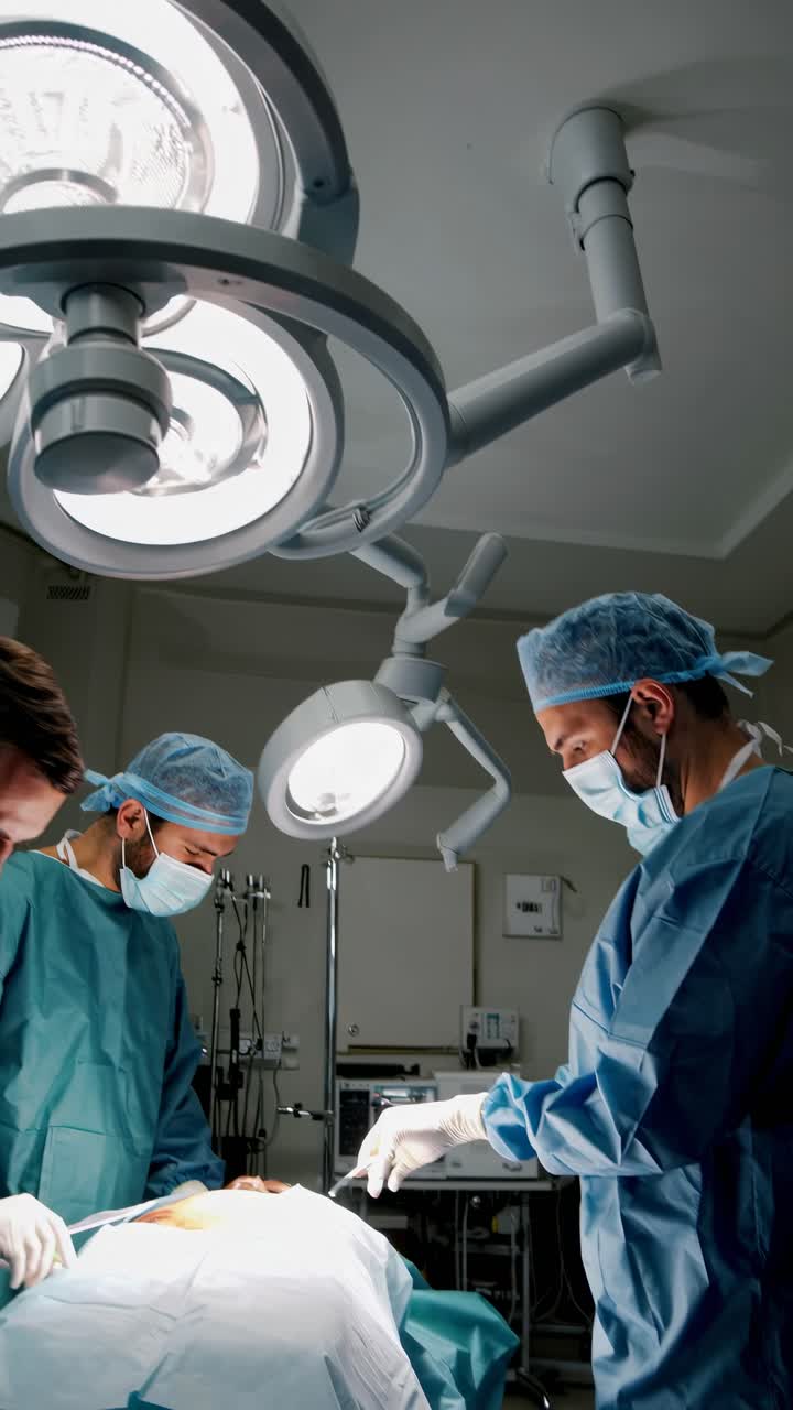 Aerial video angle captures surgeons in a sterile operating room, focused under bright surgical