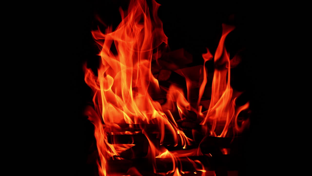 Bastoncini di legno impilati in un'alta catasta che bruciano nella notte buia. Lunghe fiamme rosse si innalzano