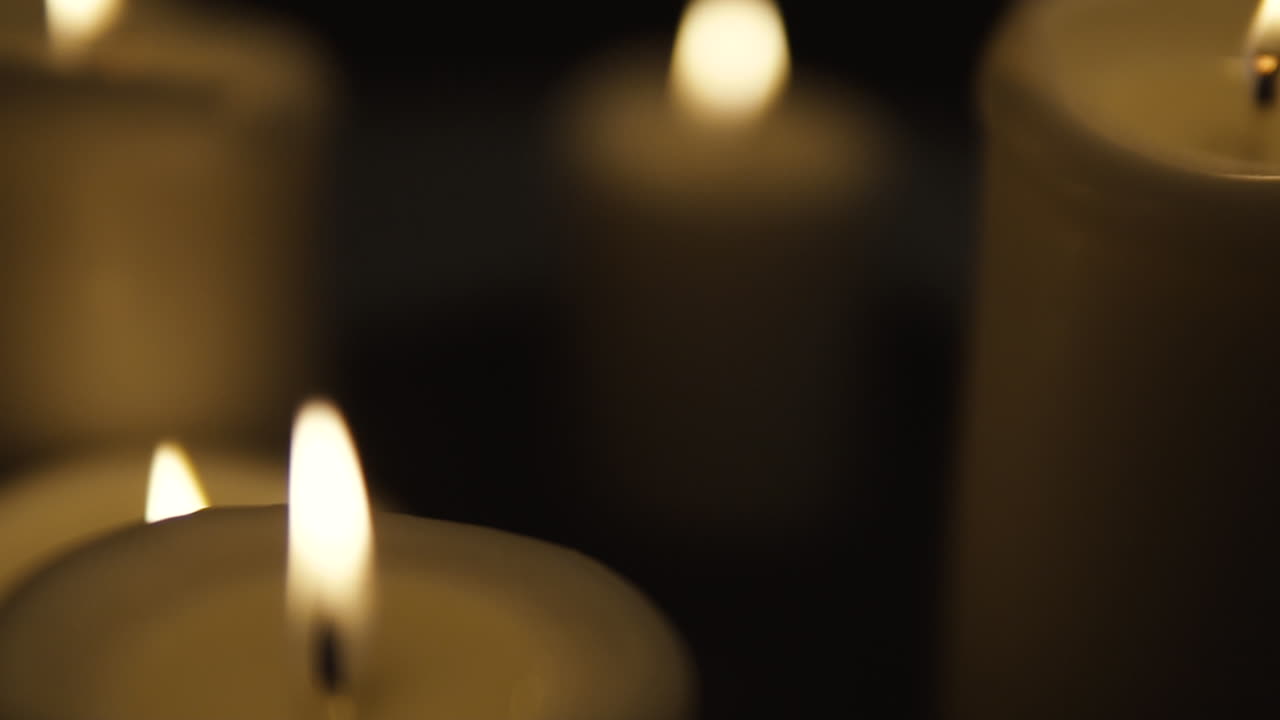 transición de derecha a izquierda, velas encendidas ocupan toda la zona, composición sobre fondo negro, cámara lenta