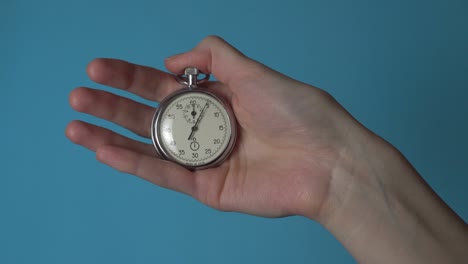 a woman's hand holds an analog stopwatch on a blue chromakey screen.