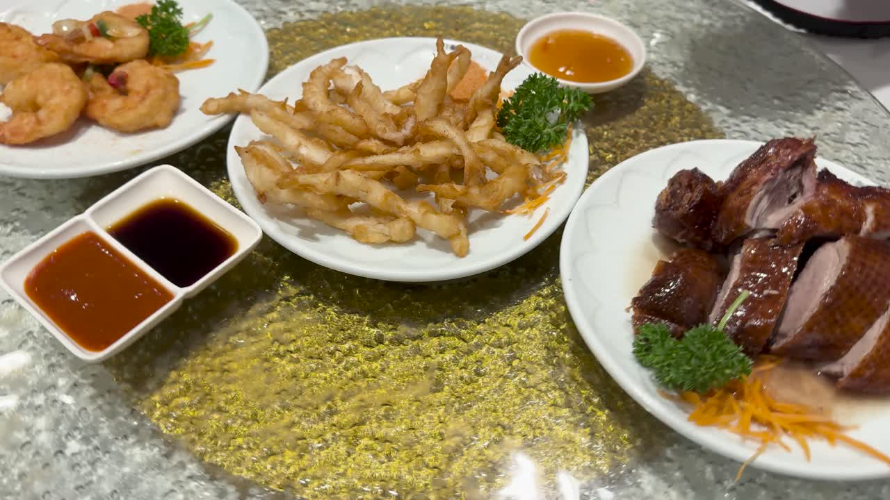 A lazy Susan rotates showcasing Chinese dim sum dishes including roast duck, battered shrimp, and whitebait with sauces