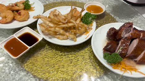 a lazy susan rotates showcasing chinese dim sum dishes including roast duck, battered shrimp, and whitebait with sauces