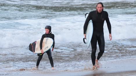 father and son walking with surfboards on beach