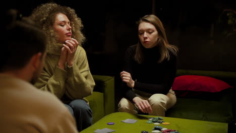 camera focuses on two women playing poker with friends