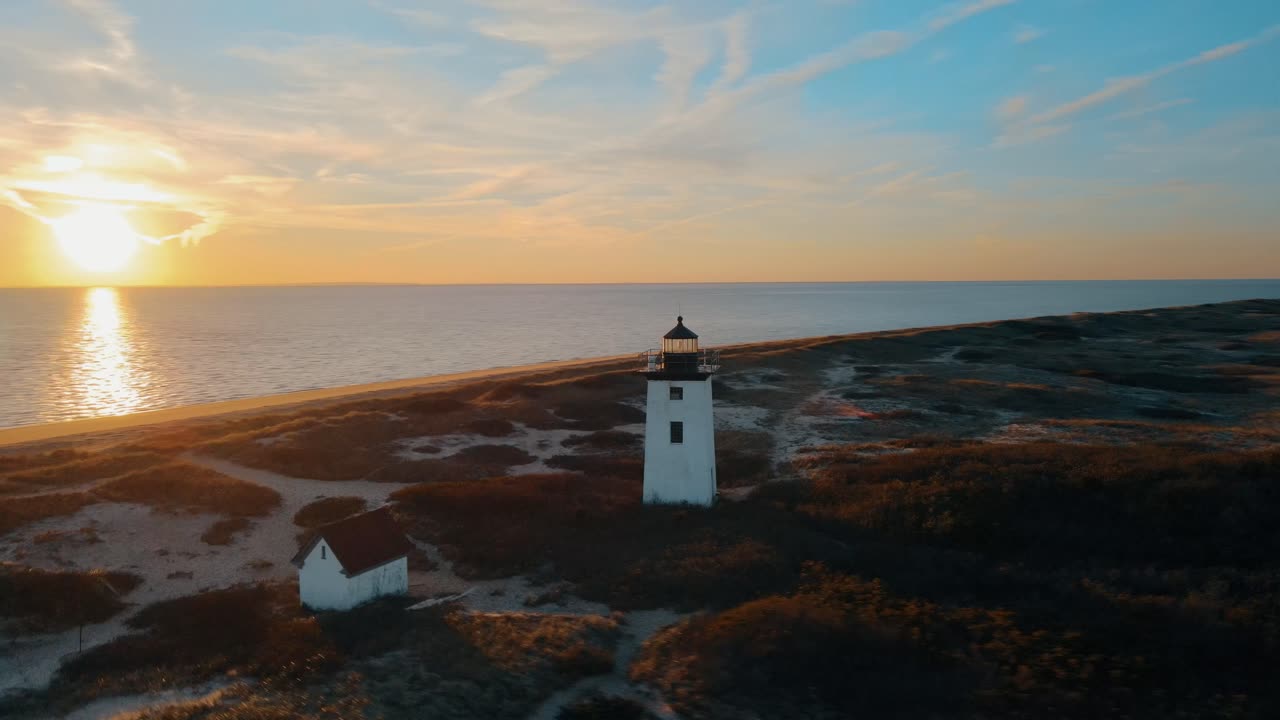 tomada aérea de órbita del faro en dunas con playa de arena y océano en provincetown estadounidense al atardecer dorado