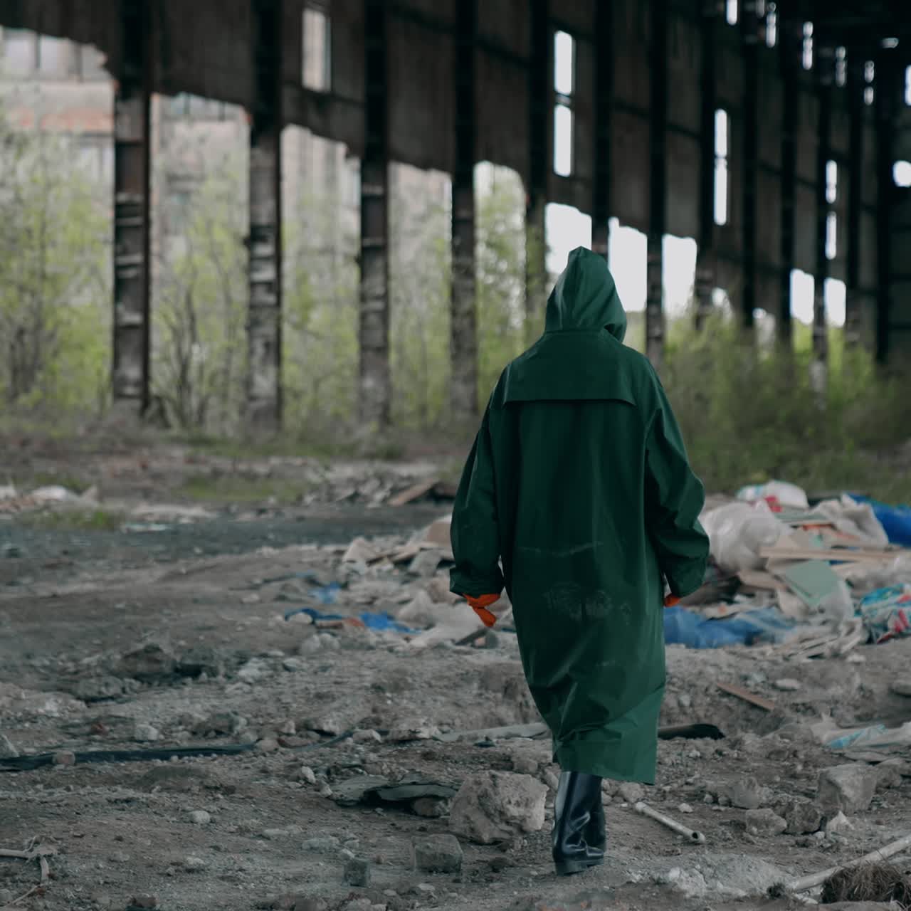 Person in abandoned place with garbage. Ecologist in protective suit walking inside the ruined building. Back view. Destructed place
