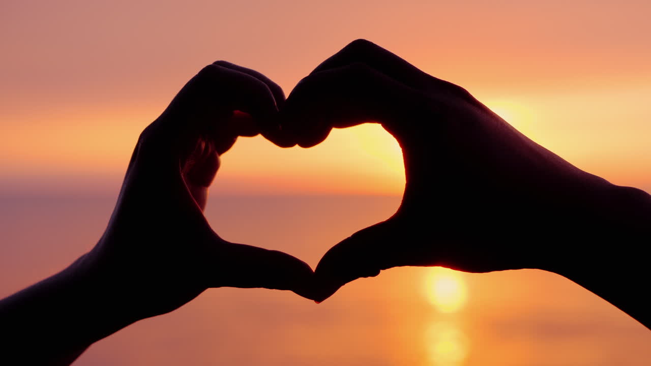 바다와 석양의 배경에 대한 하트 모양 두 팔이 함께 결합