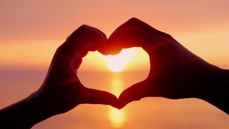 heart shape against the background of the sea and the setting sun two arms joined together