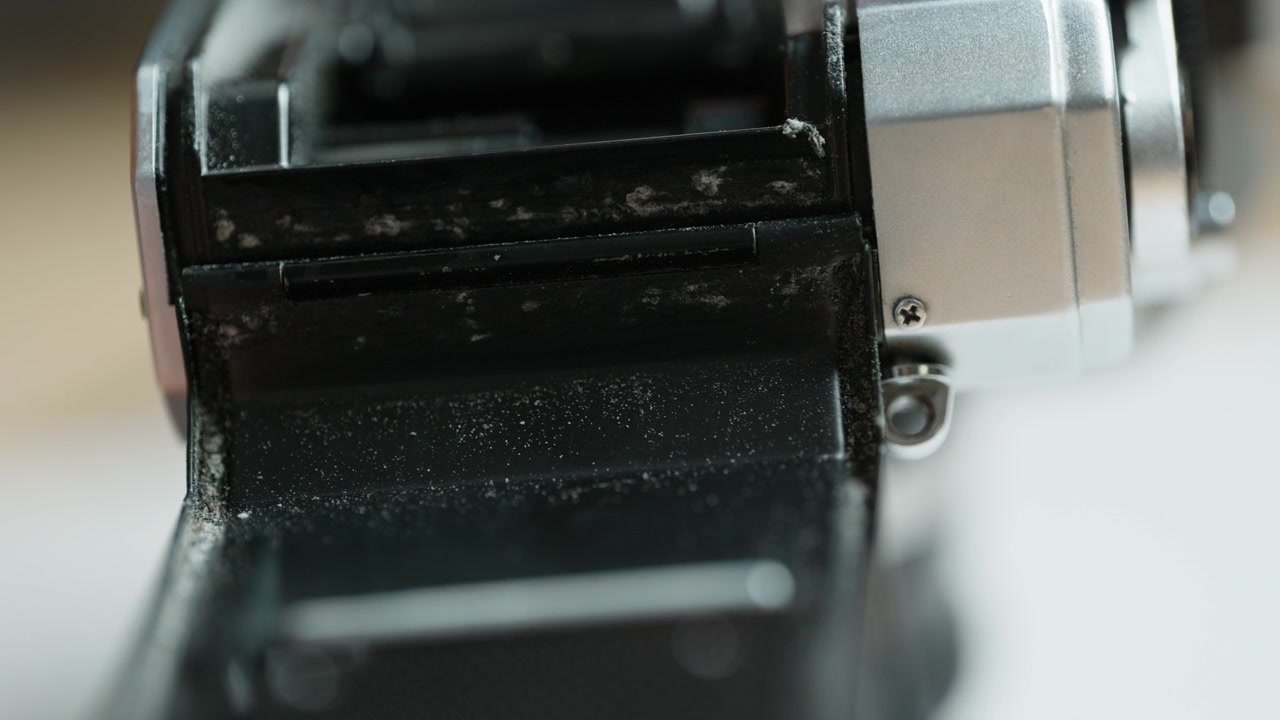 Side close-up of the light seal channel of a vintage 35mm camera being wiped with an alcohol-soaked cloth, degreasing the groove for fresh seals. A prep step of analog restoration – a clean, sound bas