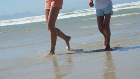 Mother-and-daughter-walking-on-shore-at-beach