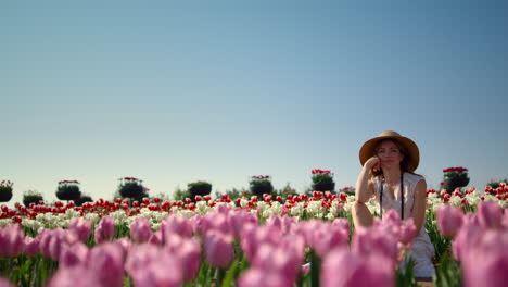 Young-gentle-woman-in-hat-enjoying-sunlight-in-blooming-floral-landscape.