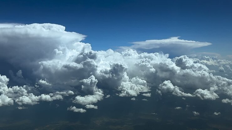 An aerial clouscape teken from a jet cockpit while flying at cruise over threatening storm clouds, with an anvil shape cumulonimbus at the back, under a blue sky.