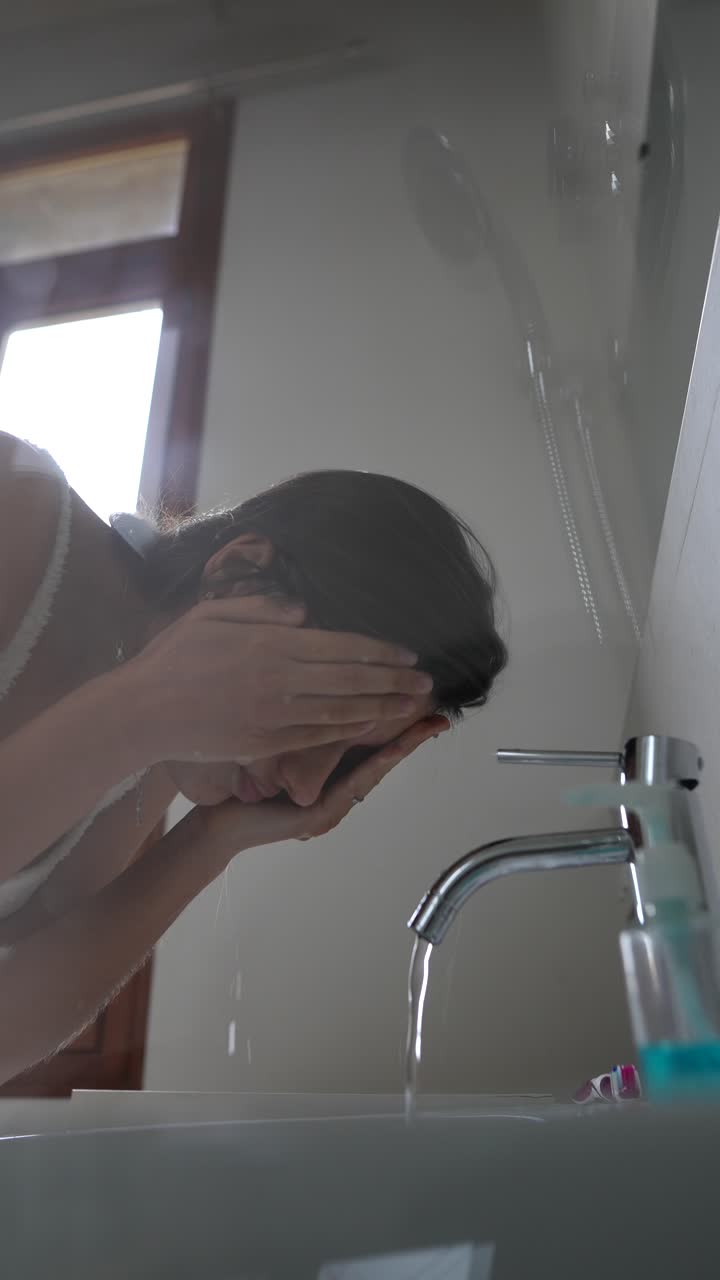 женщина моет лицо в ванной.