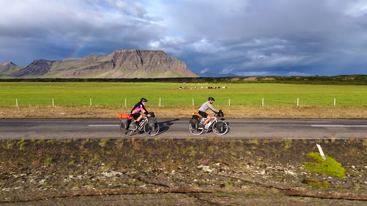 Utforskar Snæfellsneshalvön: Två cyklister på väg 54 med regnbåge och berg