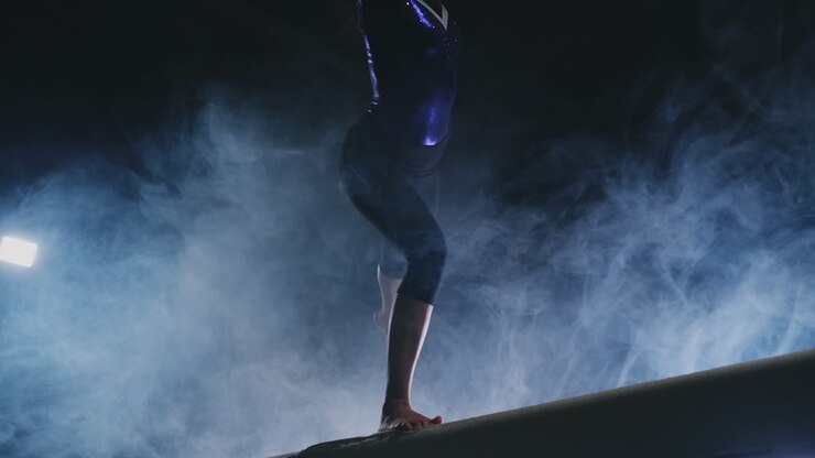 Close-up of the leg of a girl gymnast perform a balance beam jump in smoke and slow motion.