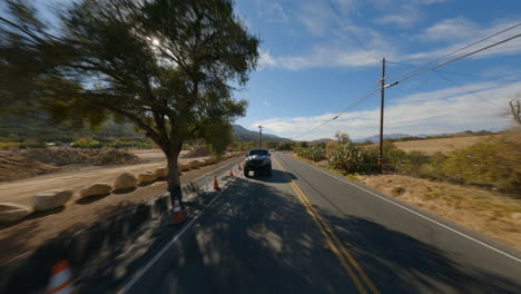 Reverse-FPV-view-of-an-off-roader-jeep-speeding-on-road-during-bright-sunny-day