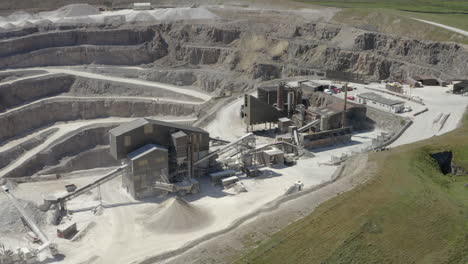 An-aerial-view-of-a-working-asphalt-quarry-building-with-the-quarry-cut-in-the-background,-Yorkshire,-UK