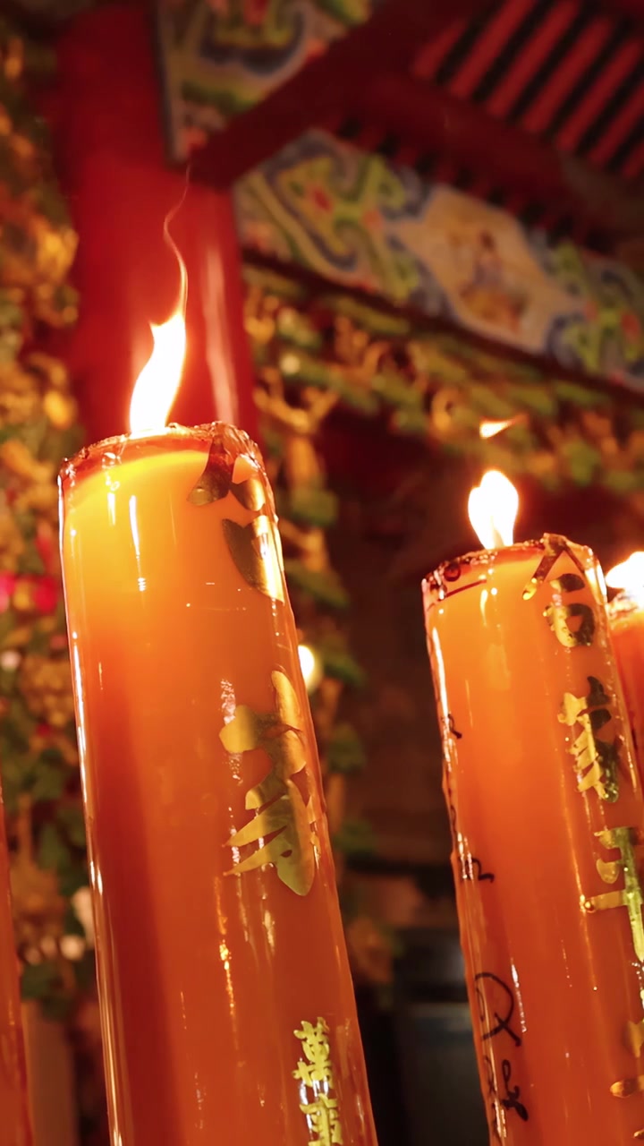 Alte candele arancioni bruciano in un tempio riccamente decorato, luce ambientale calda, lenta panoramica della telecamera.