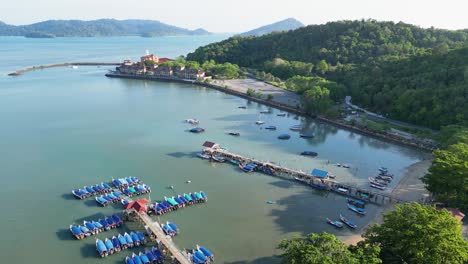 Aerial-view-of-Langkawi-pier,-Malaysia,-surrounded-by-boats,-water,-and-lush-green-hills-under-a-clear-sky