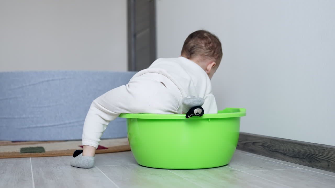 Toddler boy plays with a light green tub. Child tries to get into it and out. Rear view of a kid.