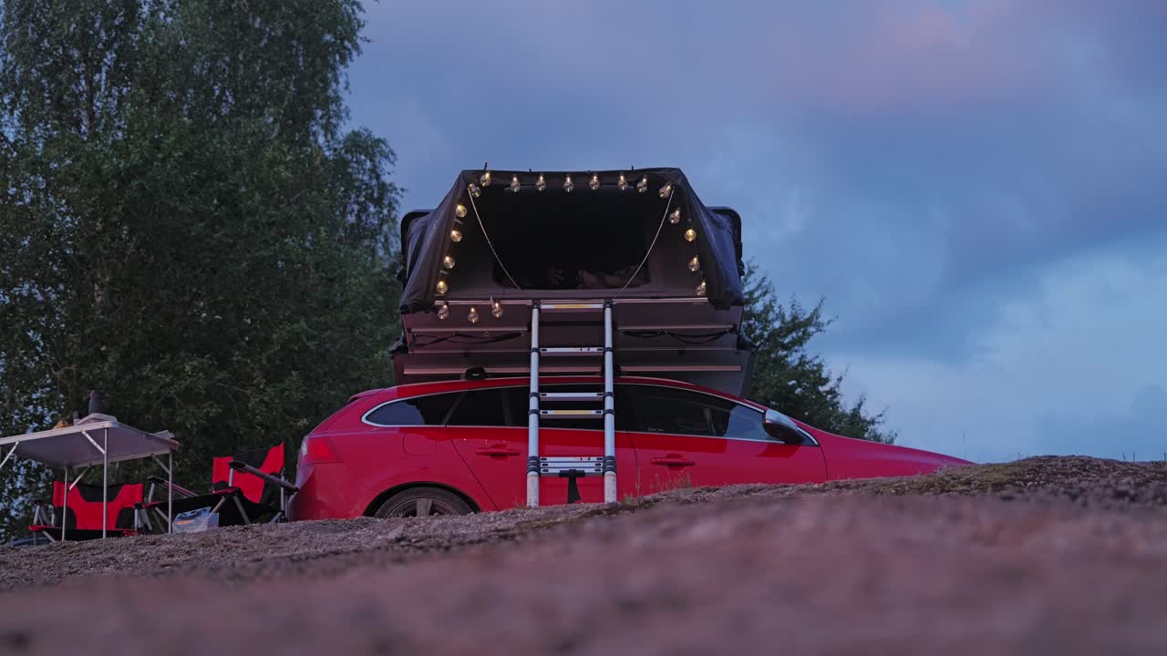 Low angle view of woman climbing ladder to rooftop tent at dusk camping