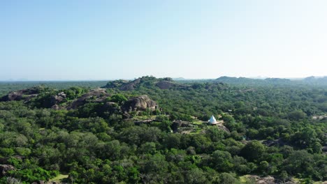 rocky outcrop in sri lanka jungle with white buddhist shrine, aerial