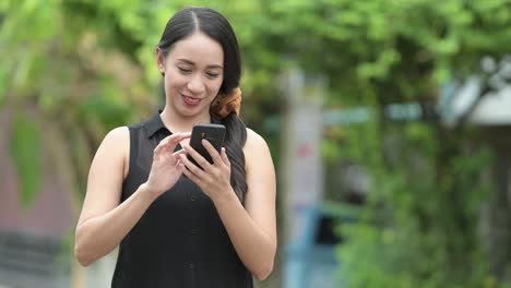 young beautiful asian businesswoman using phone in the streets outdoors