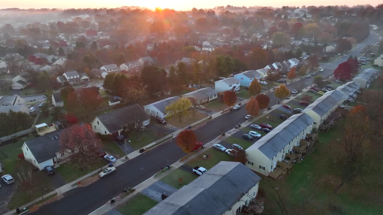 vista aérea de una calle suburbana al amanecer, con niebla, árboles de otoño, coches y casas unidas