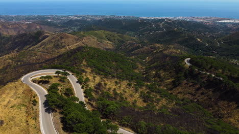 A-drone-pulls-back-over-a-mountain-road-leading-to-the-coast-near-Estepona,-Spain