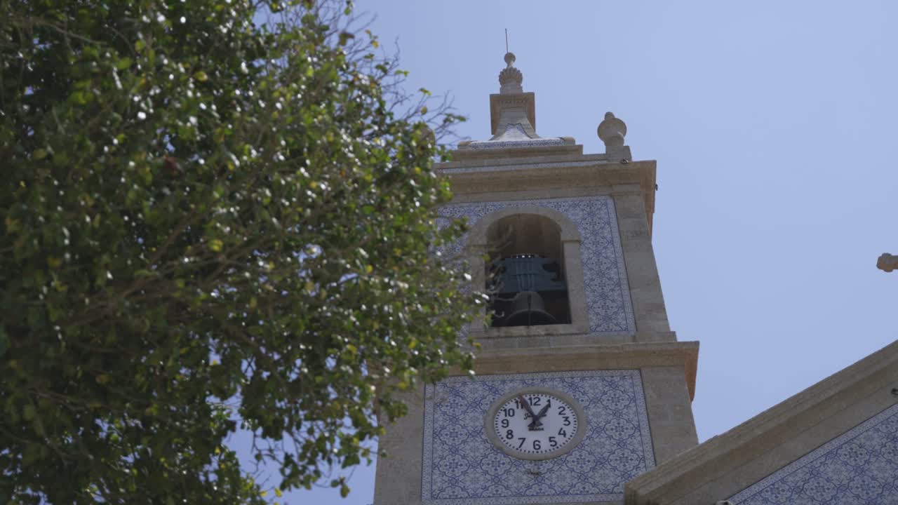 Historic tower featuring patterned blue and white tiles, a visible bell, and a round clock under bright sky