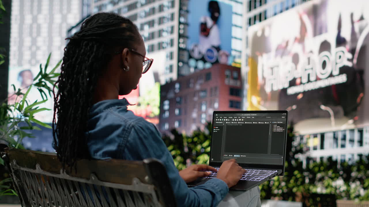 Woman software developer writing code on laptop and relaxing on park bench