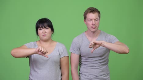 young sad multi-ethnic couple giving thumbs down together