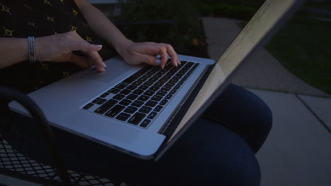 closeup of woman's hands using a laptop outside on her driveway on a summer evening