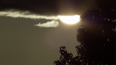 close up static shot of sun coming out from behind cloud during sunset