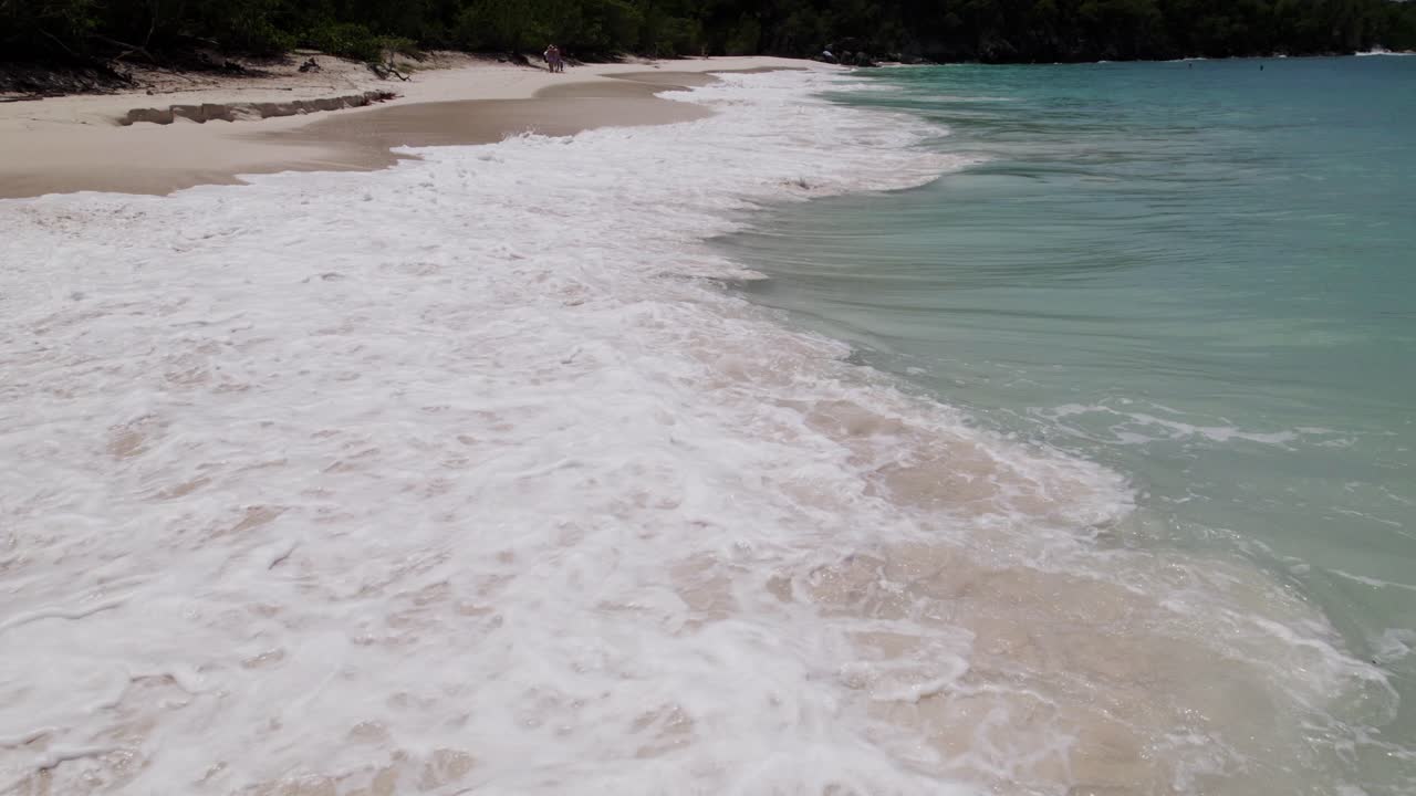 barrido aéreo tiro ancho de agua estrellándose en la playa arena de la orilla cielo azul nubes blancas agua turquesa relajación vacaciones turismo
