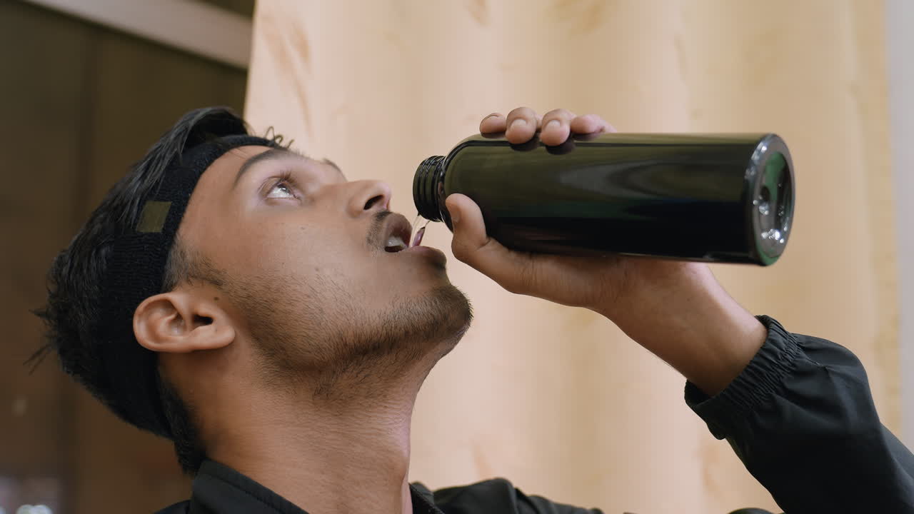 Close de um atleta bebendo água de uma garrafa preta após o treino, mostrando hidratação, refresco e momento de recuperação durante a prática esportiva, com foco na determinação